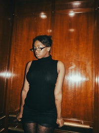 a woman in a black turtleneck dress standing in a hallway