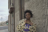 a woman in a leopard print shirt leaning against a wall